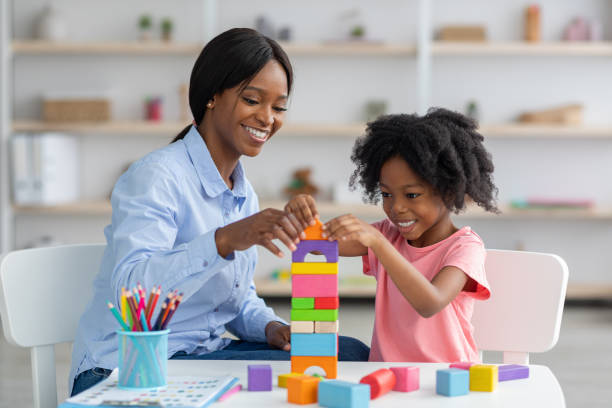 istock Adorable black kid and child development specialist playing with bricks 1369122477