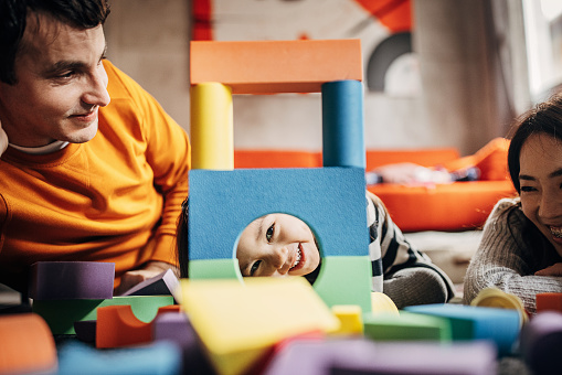 Three people, father and mother with their little daughter playing on the floor in living room.