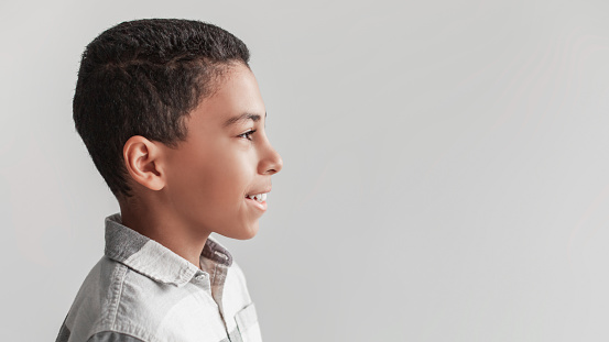 Profile Portrait Of Happy African American Boy Posing On Gray Studio Background, Wearing Shirt. Side View Of Schoolboy Standing Looking Aside At Empty Space For Text. Panorama