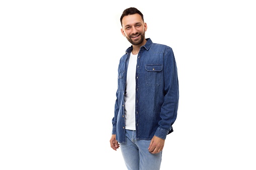 young stylish man with a beard in a denim shirt and a white t-shirt looking at the camera on a white background.