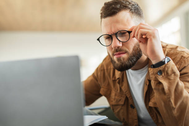 istock Man Looking At Laptop Squinting Eyes Wearing Eyeglasses Indoor 1369130271