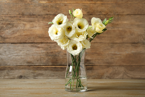 Beautiful white Eustoma flowers in vase on table against wooden background