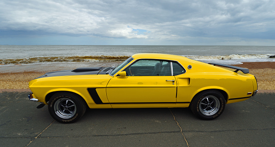 Felixstowe, Suffolk, England - May 05, 2019: Classic Yellow Ford Mustang parked on seafront promenade beach and sea in background.