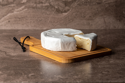 Cheese with white mold Camembert on a cutting board with a slice.