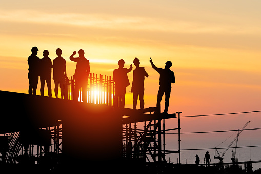 Silhouette of Engineer and worker team on building site, Industrial sector construction site at sunset in evening time