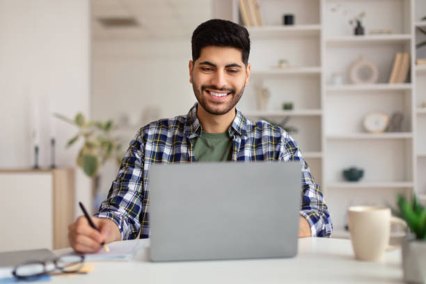 istock Portrait of smiling Arab man using laptop and writing 1369140557