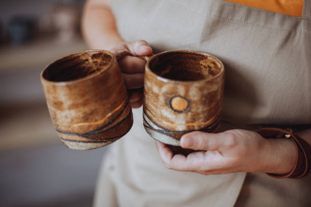 istock Woman potter holding mugs made by hand from clay 1369140911
