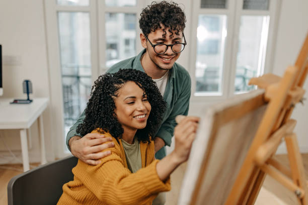 jovem casal gosta de passar um tempo juntos pintando e usando tecnologia - women heterosexual couple love men - fotografias e filmes do acervo