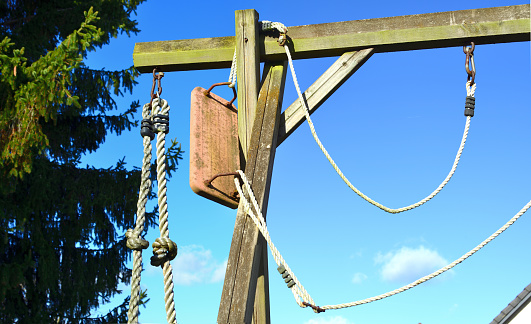 Sunny day in February. Private playground: Seat and cords hanging on top of the corner of the wooden beam structure