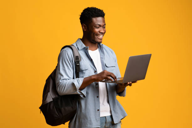 Smiling african american male student using laptop stock photo