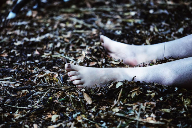 葉のごみの間で森の床に横たわっている死んだ人の足と足 - 殺人 ストックフォトと画像