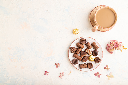 Chocolate candies with cup of coffee and hydrangea flowers on a white concrete background. top view, flat lay, copy space.