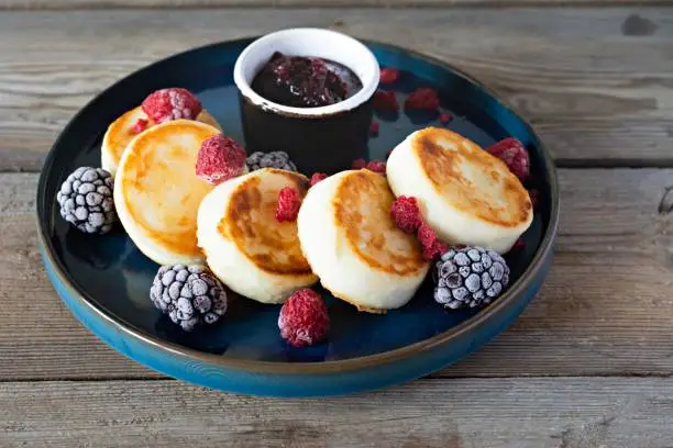 Fresh cottage cheese or ricotta  pancakes (syrniki,fritters) on a blue plate with fresh berries and jam. Delicious healthy cottage cheese breakfast.  Ukrainian, Russian cuisine sweet food