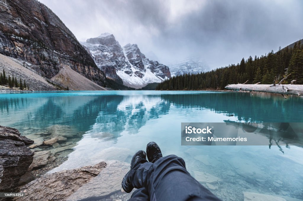 Legs of traveler relaxing on Moraine Lake with rocky mountains in gloomy day at Banff national park Legs of traveler relaxing on Moraine Lake with rocky mountains in gloomy day at Banff national park, Alberta, Canada Hiking Stock Photo