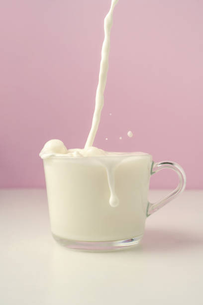 istock Milk is poured into a transparent cup on a purple background. 1369156383