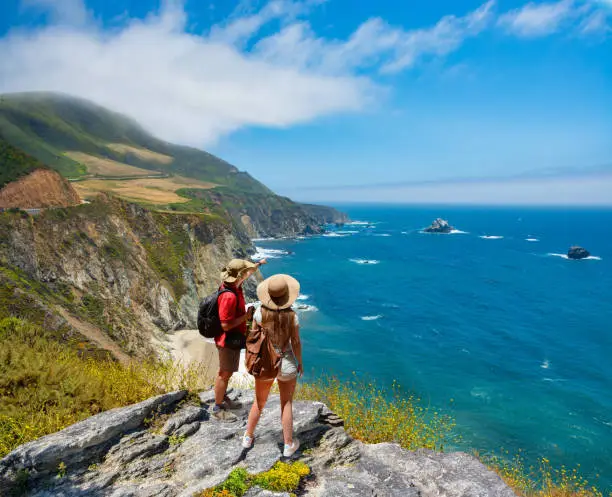 Photo of Couple on hiking trip resting on top of the mountain looking at ocean view.