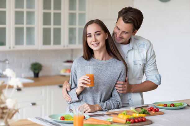 casal romântico jovem apaixonado, homem e mulher abraçados e se divertindo juntos na cozinha de casa. vida de casal - carrot juice - fotografias e filmes do acervo