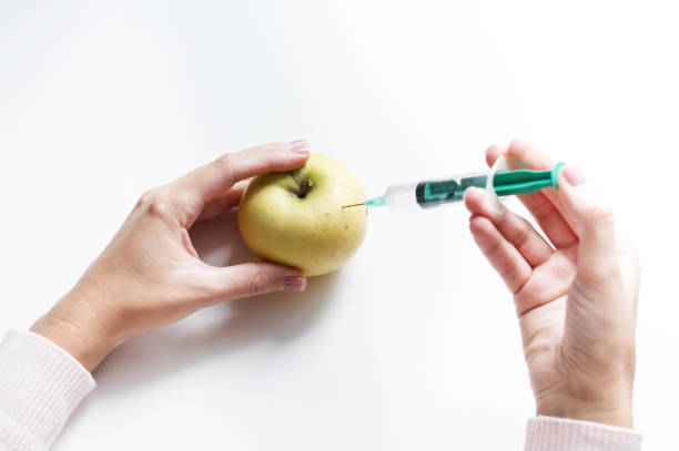 inyección de jeringa en una manzana con ácido sórbico a la espera del almacenamiento a largo plazo de la fruta. alimentos genéticamente modificados. aislado sobre fondo blanco - food crop sprayer insecticide dna fotografías e imágenes de stock