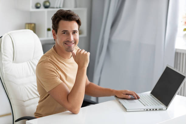istock Young smiling man with a laptop at the table. Freelancer, remote work 1369158927