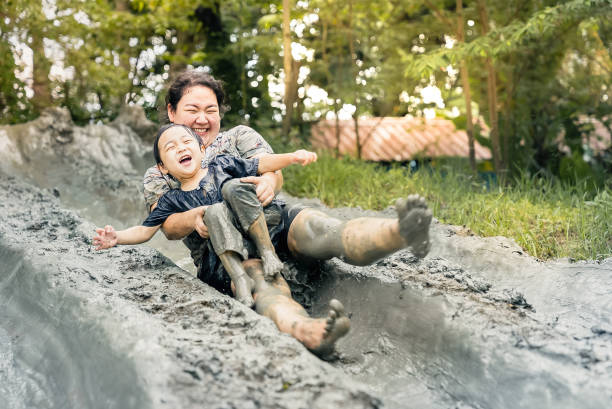 Asian happy mother and child have activities together on holidays. Mom and her son playing slider that made from mud. Happy harmonious family outdoors and learning concept. stock photo