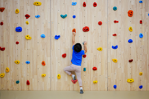 Little boy climbing a rock wall indoor.