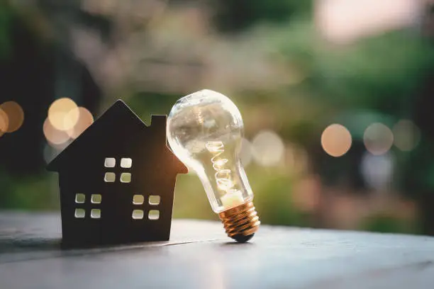 Photo of Light bulb with wood house on the table, a symbol for construction, Creative light bulb idea, power energy or business idea concept ecology, loan, mortgage, property or home.