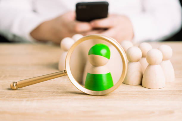 A magnifying glass and a green wooden figures with blur business man uses mobile phones search for someone who ‘s special person. Concept of Human resources management and recruitment. stock photo