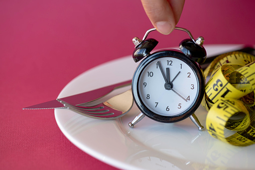 Measuring tape in empty plate with alarm clock. Woman holding alarm clock.