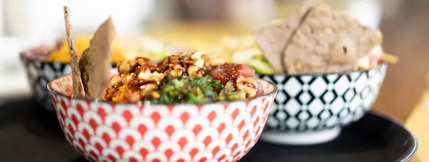 Photo of Horizontal banner or header with bowl of poke or marinated seasoned raw fish on a table in a modern fusion restaurant - Typical Hawaiian dish and international cuisine concept