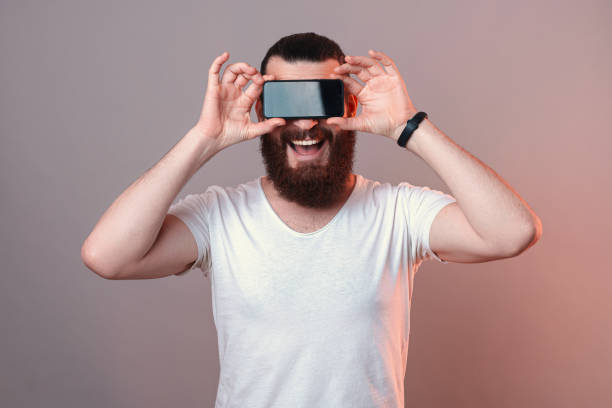 Excited bearded man is covering his eyes while standing over grey and red background.