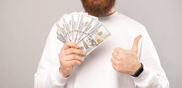 Close up photo of man holding money and showing thumb up stock photo