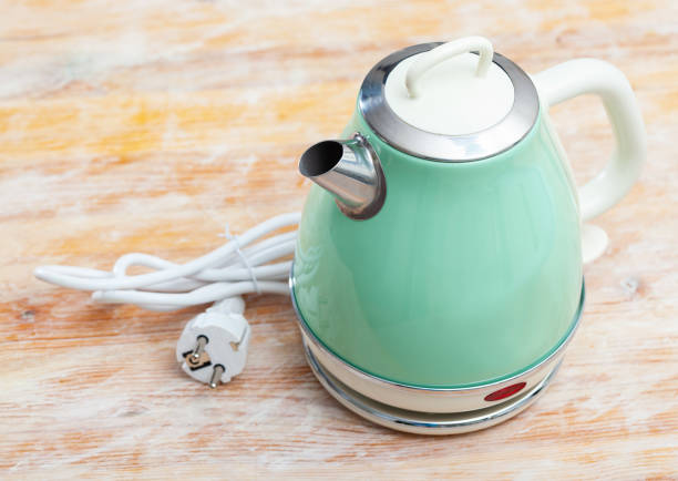 Metal light green electric kettle with vintage design reminiscent of old fashioned shapes on wooden surface