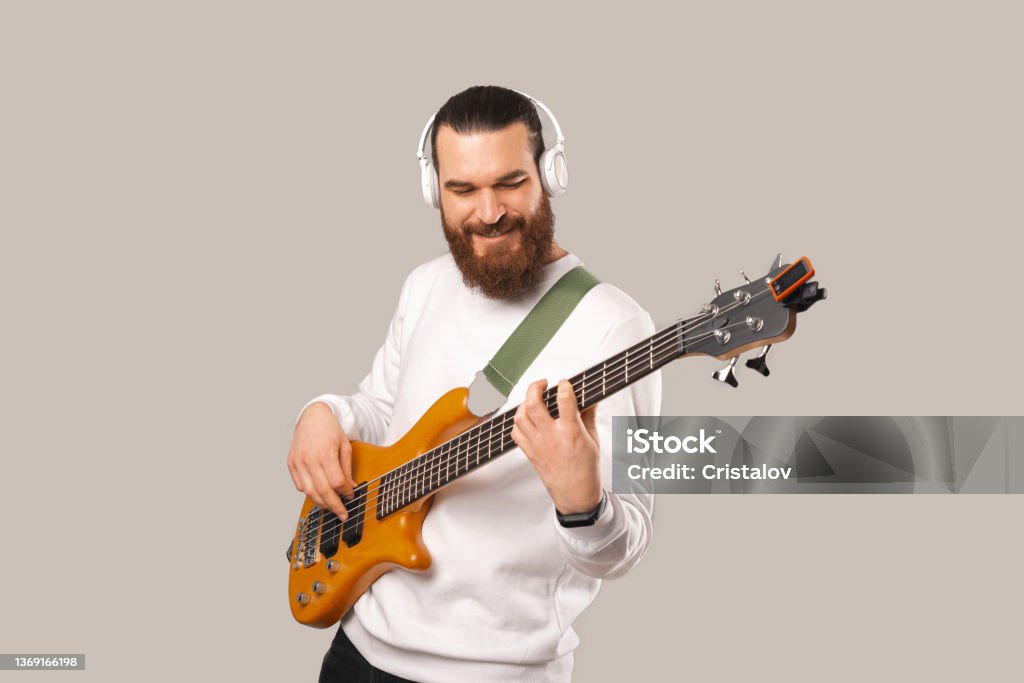 Photo of young handsome bearded man playing at bass guitar with 5 strings Photo of young handsome bearded man playing at bass guitar with 5 strings. Bass Guitar Stock Photo