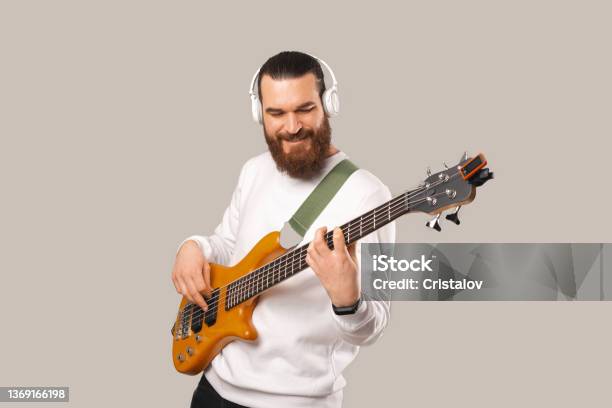 Photo Of Young Handsome Bearded Man Playing At Bass Guitar With 5 Strings Stock Photo - Download Image Now