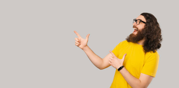 istock Hey look at this. Excited bearded man pointing at the corner over grey background 1369166212