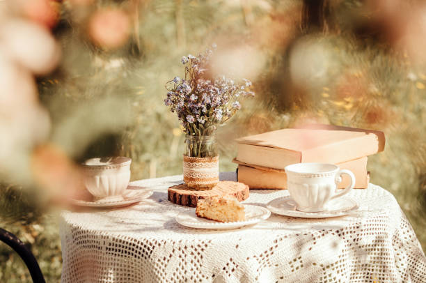 istock Dream like view through apple blossoms to table, set with tea cups and books. Bouquet of wildflowers Myosotis arvensis forget me nots in handmade jar vase. 1369166313