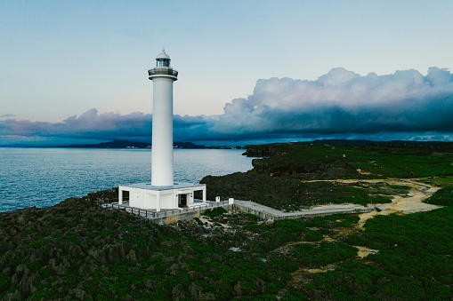 White lighthouse on ocean cliff coastline clouds captured by drone in Okinawa, Okinawa, Japan