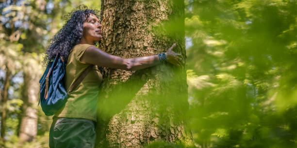 istock Curly haired Hispanic woman giving hug to tree trunk in forest 1369167617