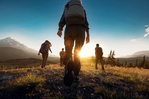 Group of sporty people walks in mountains at sunset with backpacks
