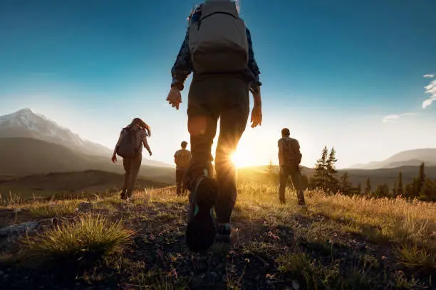Photo of Group of sporty people walks in mountains at sunset with backpacks