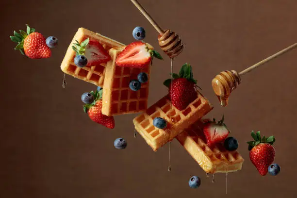 Waffles with blueberries and strawberries are watered with honey. Food levitation. Copy space.