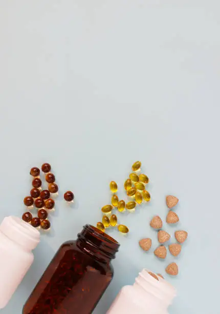 Photo of Different tablets, capsules, pills are scattered from the jar on a light background The concept of health Minimalism