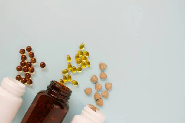 Photo of Different tablets, capsules, pills are scattered from the jar on a light background The concept of health Minimalism