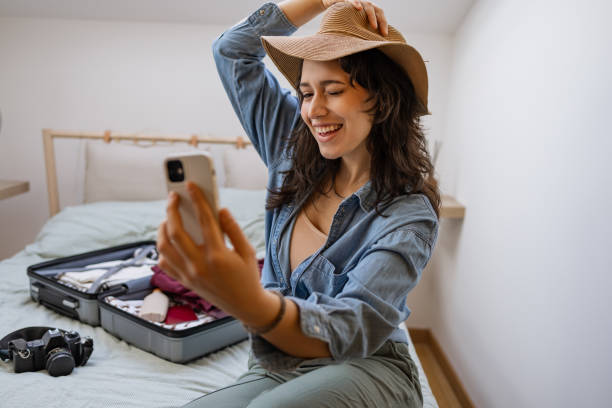 istock Young woman sitting on the bed, taking a selfie while preparing for a trip 1369173008