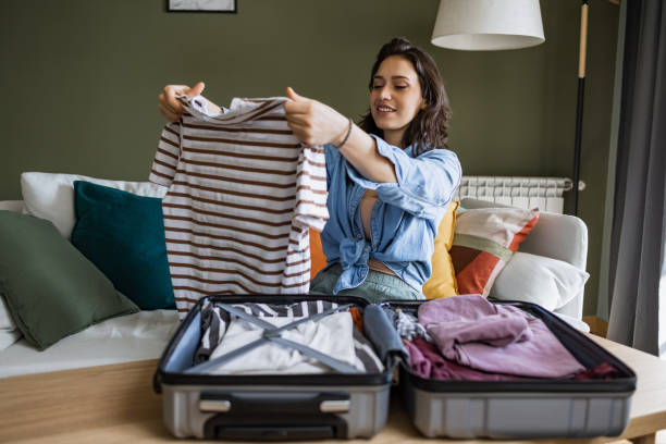 istock Young woman sitting on the couch and stacking clothes in a suitcase 1369173872