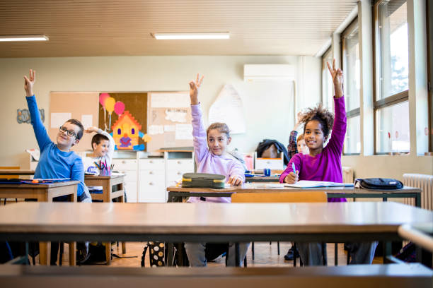 istock Schoolchildren at classroom with raised hands answering teacher's question. 1369175482
