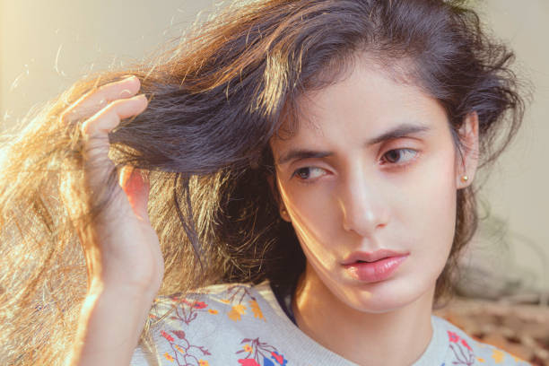 Young woman looks at her hair sadly. In this indoor portrait shot at night emanating daylight portrait, an Asian/Indian, beautiful young woman holds her entangled falling hair in hand with worries. pale complexion stock pictures, royalty-free photos & images