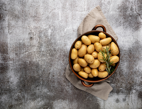 Raw small potatoes in a cast iron pan on a beton background.