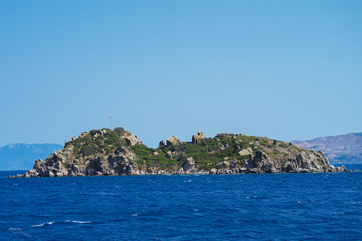 View of a small uninhabited rocky island with a cell tower in the Aegean Sea, Turkey.