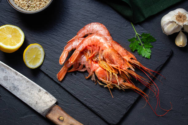 top view of a bunch of prawns with lemon, garlic and parsley on slate table